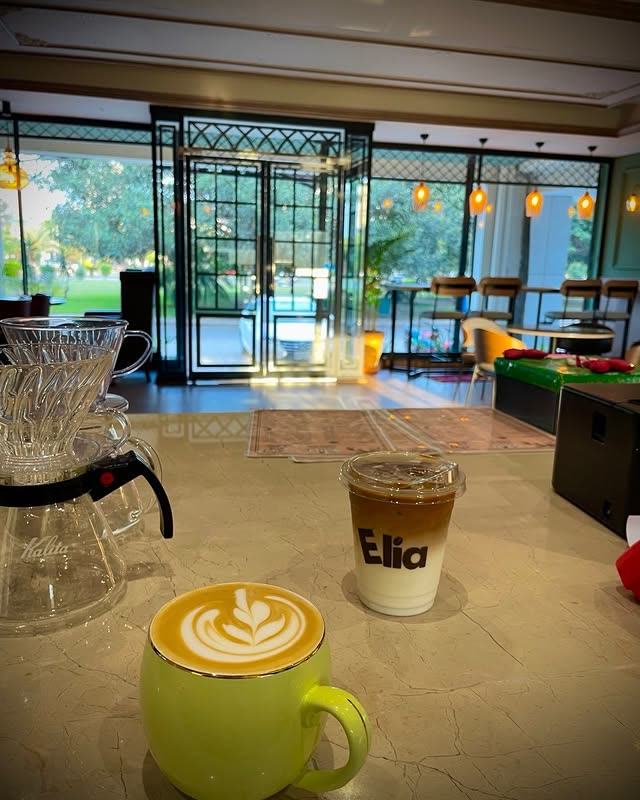 A latte with rosetta art beside an iced Elia coffee, the geometric front door of the cafe behind
